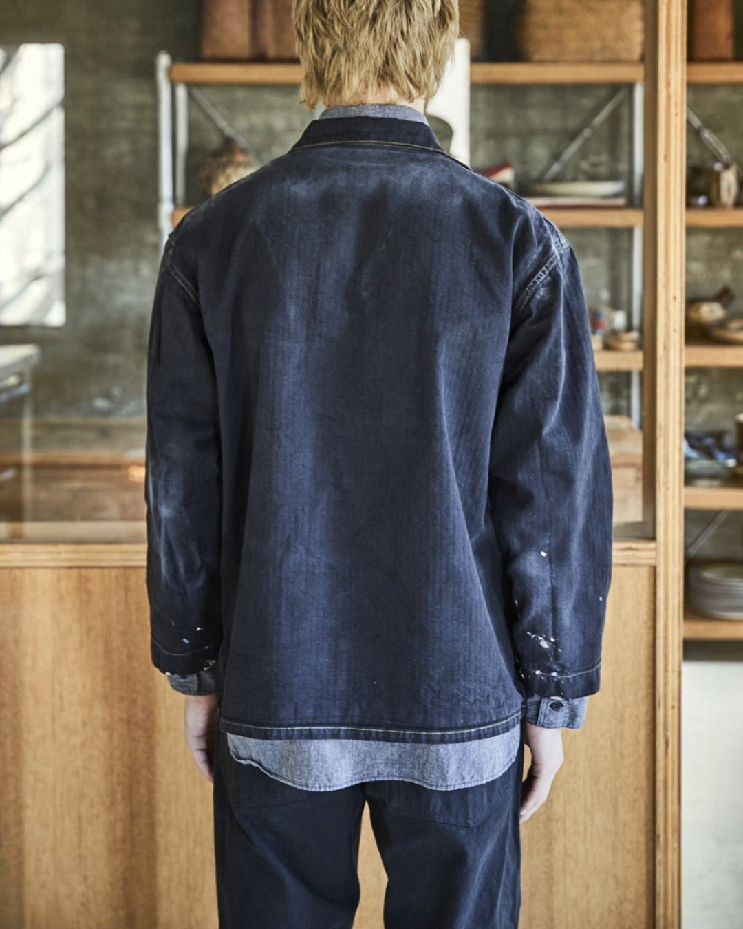 Vue de dos d'un homme portant la veste OrSlow Remade Herringbone Coverall noire en coton avec des éclaboussures