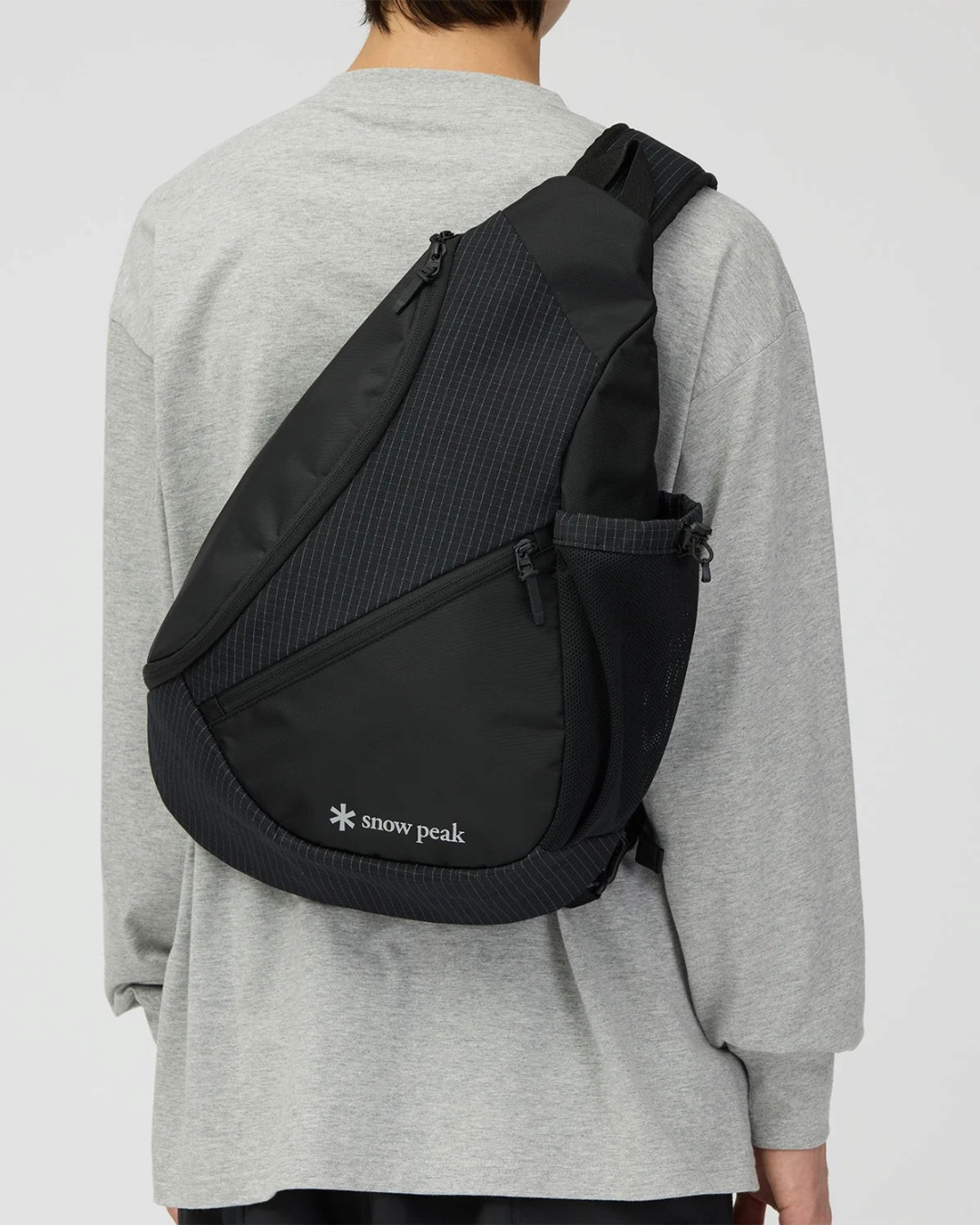 Sac bandoulière noir Snow Peak en tissu ripstop quadrillé avec poches latérales en filet porté par un mannequin
