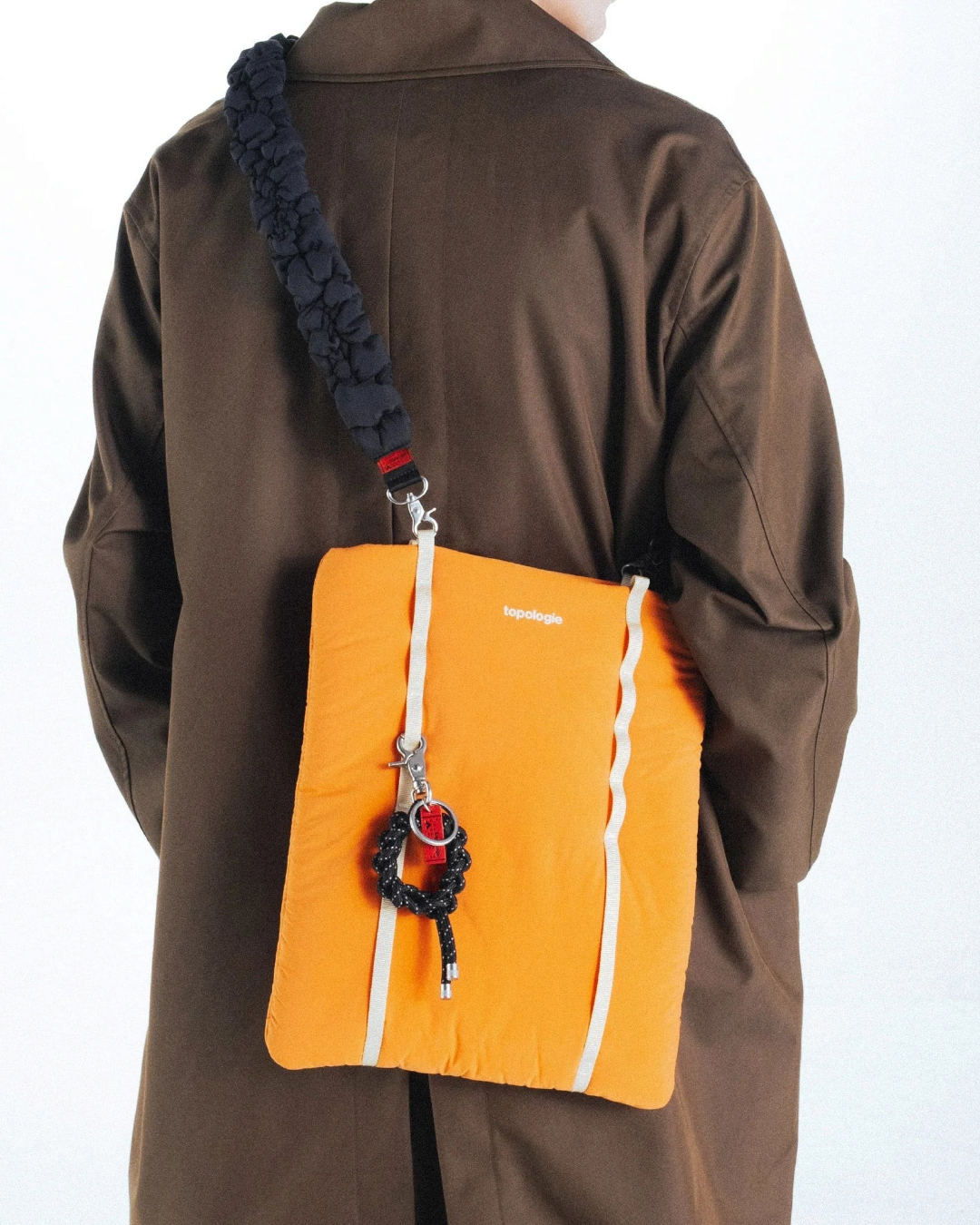 Porte-clés noir Topologie Krans en corde tressée attaché à un sac orange Merci Paris porté par un homme