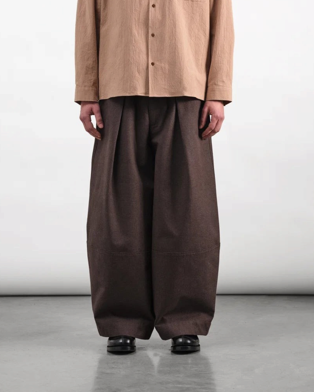 Homme portant le pantalon Deadbeat marron de Merci Paris avec une coupe large, taille haute et plis marqués