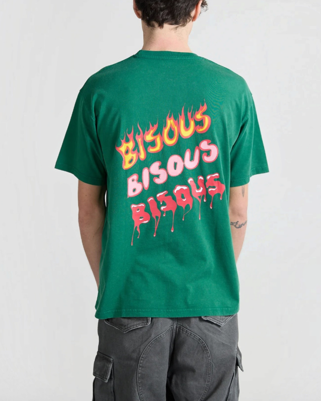 Homme portant un t-shirt vert Merci Paris Bisous Skateboard avec imprimé graphique flammes et coulures au dos