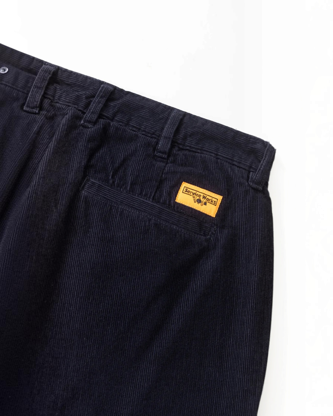 Pantalon en velours bleu marine Service Works avec poches et étiquette orange, disponible chez Merci Paris